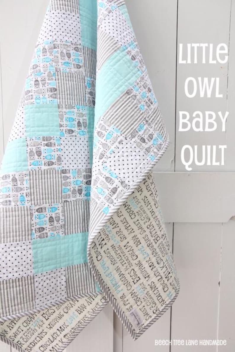 May include: A handmade baby quilt with a patchwork design. The quilt features squares of blue, gray, and white fabrics with owl and stripe patterns. The border has text. The words "Little Owl Baby Quilt" are visible.