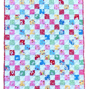 May include: A colorful patchwork quilt with a red border. The quilt is made of small squares in various colors, including red, blue, pink, yellow, and green, with floral and patterned designs. The quilt is quilted with white thread.