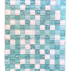 May include: A handmade quilt with a patchwork design. The quilt features a grid pattern of alternating squares in shades of teal and white. Some teal squares have a pattern of small white animals. The quilt is edged with a teal border.