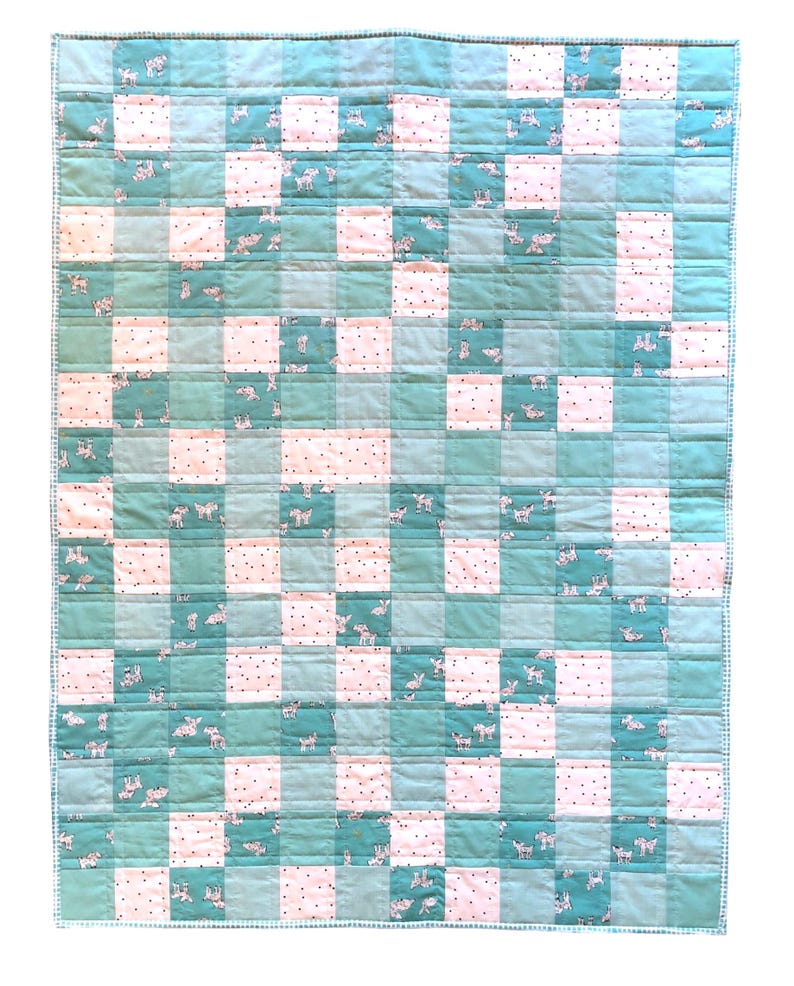 May include: A handmade quilt with a patchwork design. The quilt features a grid pattern of alternating squares in shades of teal and white. Some teal squares have a pattern of small white animals. The quilt is edged with a teal border.