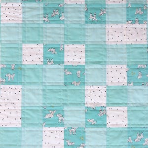 May include: A patchwork quilt featuring a repeating pattern of squares. The quilt alternates between light blue squares, white squares with black polka dots, and squares with a dog print. The quilt is machine-stitched with a grid pattern.