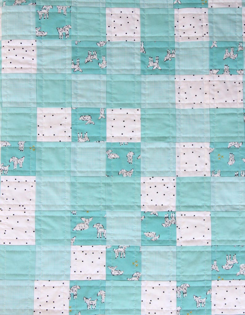 May include: A patchwork quilt featuring a repeating pattern of squares. The quilt alternates between light blue squares, white squares with black polka dots, and squares with a dog print. The quilt is machine-stitched with a grid pattern.