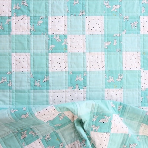 May include: A handmade quilt with a patchwork design. The quilt features squares of white fabric with black polka dots and light blue squares with a repeating pattern of white and gray animal illustrations. The quilt is folded over at the bottom.