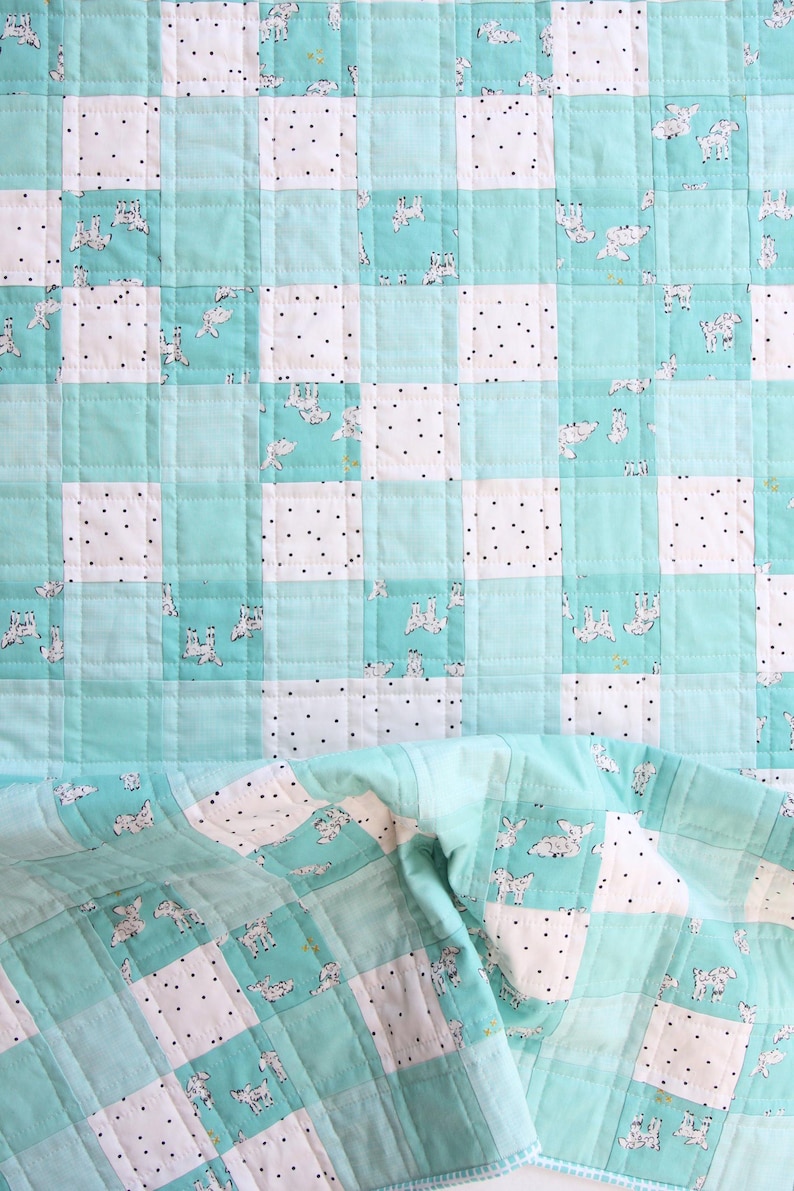 May include: A handmade quilt with a patchwork design. The quilt features squares of white fabric with black polka dots and light blue squares with a repeating pattern of white and gray animal illustrations. The quilt is folded over at the bottom.