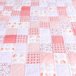 May include: A patchwork quilt featuring a variety of pink and white fabrics. The quilt is composed of numerous squares, some solid pink, others with floral or dotted patterns. The edges are finished with a red and white striped border.