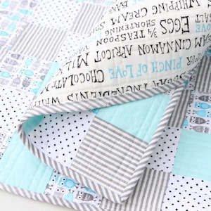 May include: A patchwork quilt with a mix of patterns, including stripes, polka dots, and owl motifs. The quilt features a light blue, gray, and white color scheme. The edge of the quilt has text that reads "Ingredients".