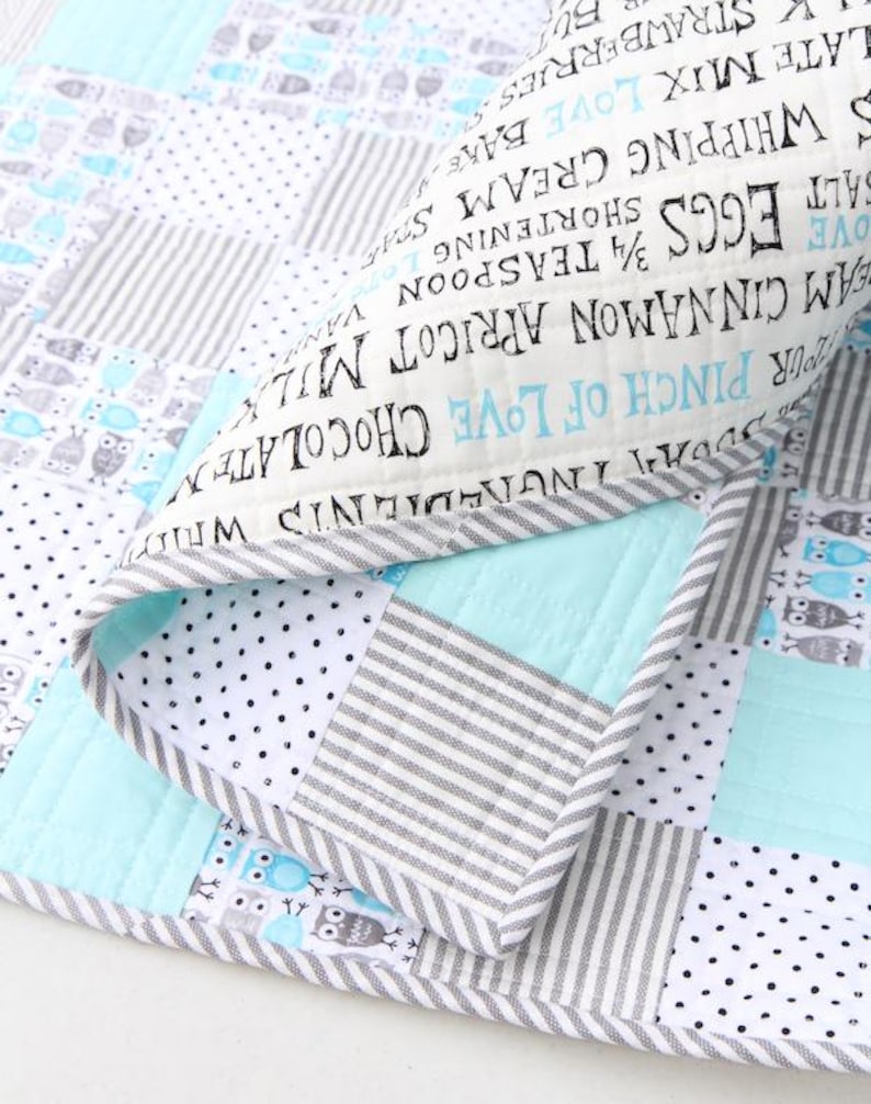 May include: A patchwork quilt with a mix of patterns, including stripes, polka dots, and owl motifs. The quilt features a light blue, gray, and white color scheme. The edge of the quilt has text that reads "Ingredients".
