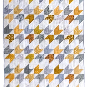 May include: A handmade quilt with a repeating geometric pattern. The design features white, gray, mustard yellow, and brown fabric pieces arranged in a diagonal pattern. The quilt is bordered with a blue and white gingham fabric.