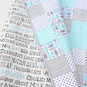 May include: A patchwork quilt with a mix of patterns, including owls, stripes, polka dots, and solid squares in shades of blue, gray, and white. The quilt has text printed on the fabric.