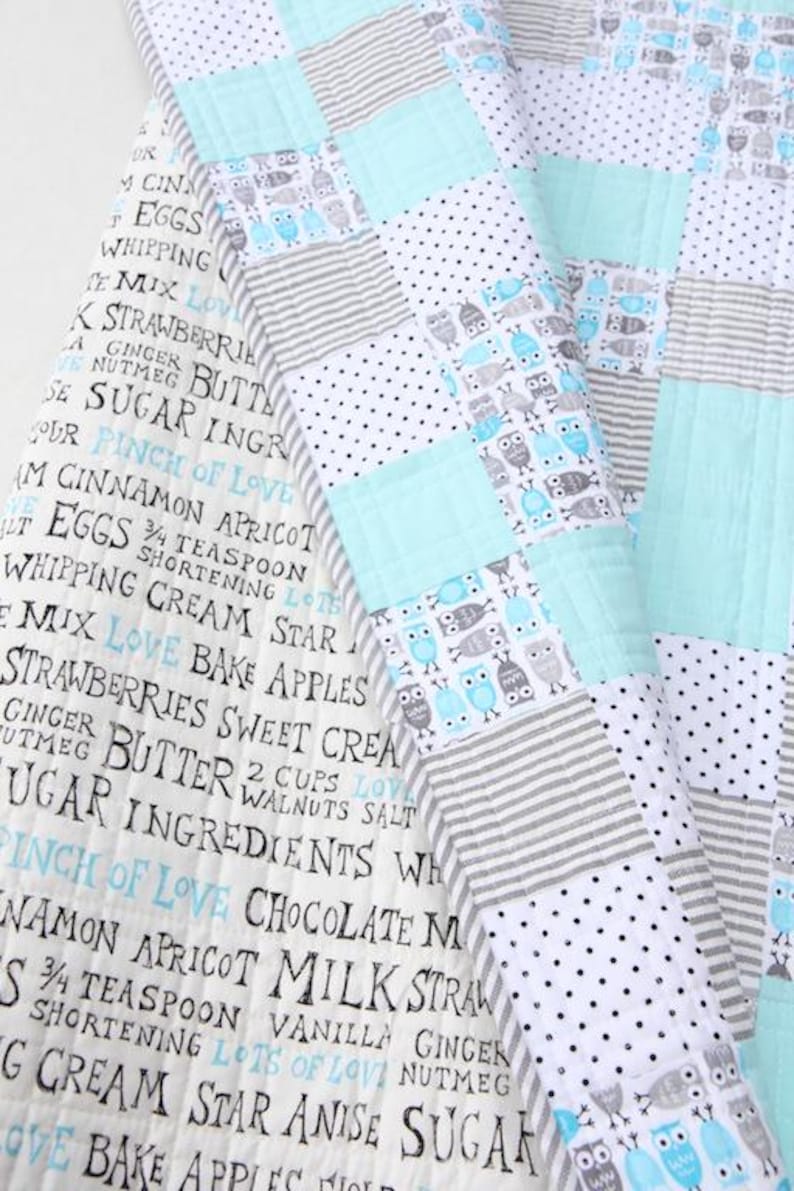 May include: A patchwork quilt with a mix of patterns, including owls, stripes, polka dots, and solid squares in shades of blue, gray, and white. The quilt has text printed on the fabric.