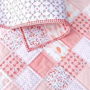 May include: A pink and white patchwork quilt and pillow set. The quilt is made up of squares with floral and leaf patterns. The pillow has a white background with a repeating floral design and a red border. The quilt is likely 150cm x 200cm.