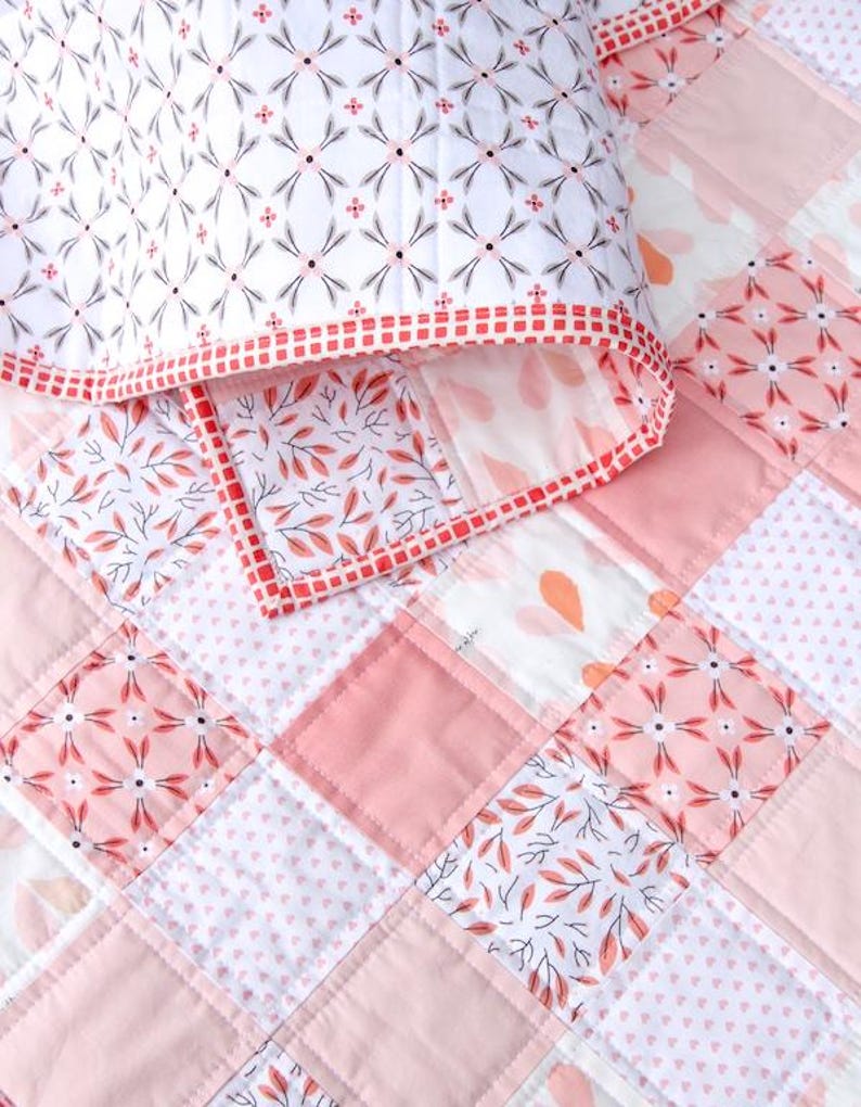 May include: A patchwork quilt and pillow set in shades of pink and white. The quilt features a geometric pattern of squares with floral and leaf designs. The pillow has a white background with a repeating floral pattern and a red border.