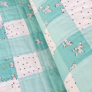 May include: A close-up of a handmade quilt with a patchwork design. The quilt features squares of white fabric with black polka dots, and light blue squares with a sheep pattern. The quilt is folded over, showing the quilted texture.