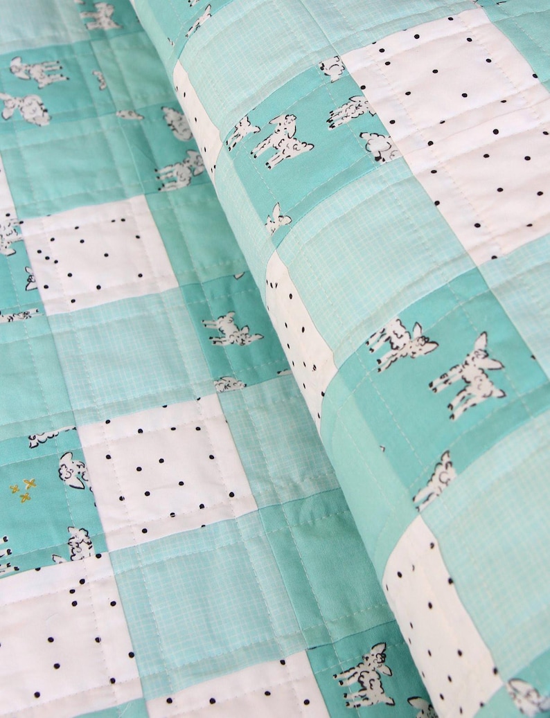 May include: A close-up of a handmade quilt with a patchwork design. The quilt features squares of white fabric with black polka dots, and light blue squares with a sheep pattern. The quilt is folded over, showing the quilted texture.