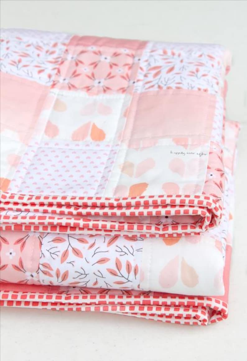 May include: Folded patchwork quilt in shades of pink, white, and coral. The quilt features floral and geometric patterns, with a red and white checkered border. The text "happily ever after" is visible on one of the quilt squares.