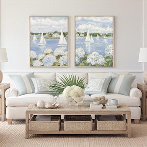 May include: A coastal-themed living room with a white sofa, light blue pillows, and two framed paintings of sailboats on the water. A woven coffee table with storage baskets sits in front of the sofa. Two beige lamps are on side tables.