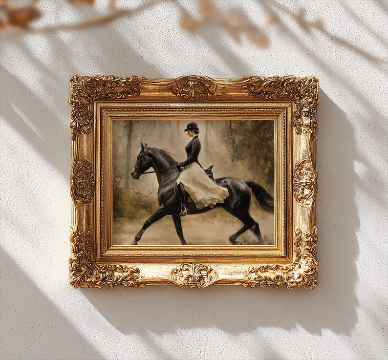 May include: A framed painting depicting a rider in a black jacket and hat on a black horse, wearing a long cream-colored skirt. The artwork is encased in an ornate, rectangular gold frame with intricate relief carvings along the edges.