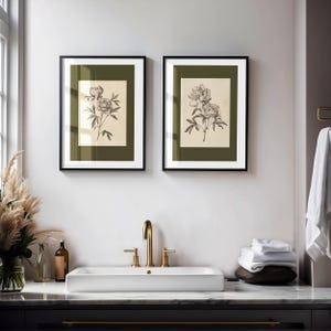 Set of two vintage botanical peony wall art prints in gold frames with green matting, styled above a farmhouse kitchen sink with brass fixtures and white hydrangeas in a soft blue cottage-style kitchen.