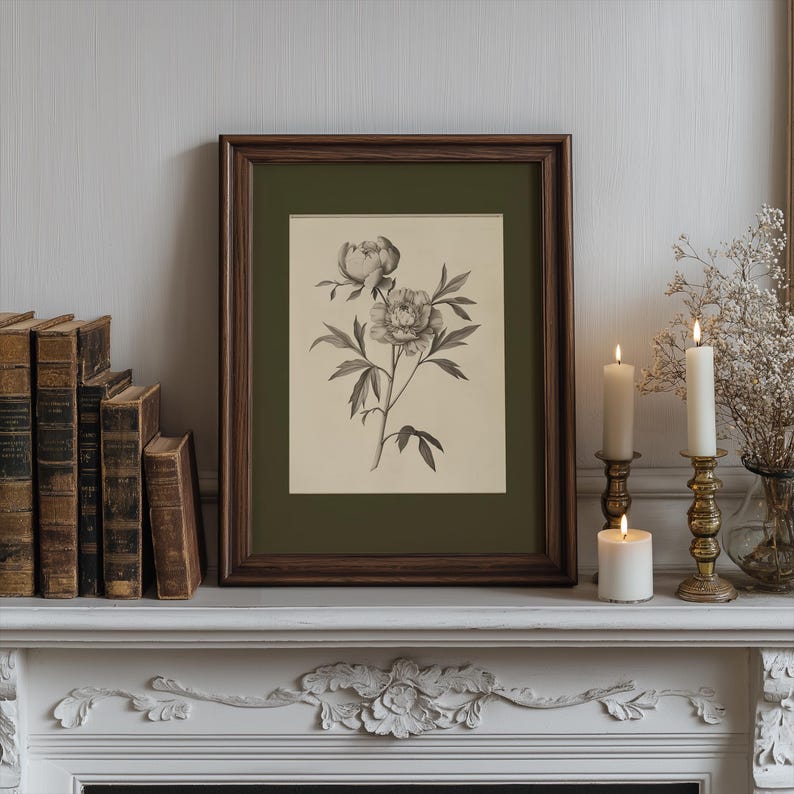 以下が含まれることがあります： 暗い木製のフレームに入ったシャクヤクの花の額入り植物画。このプリントは、白いマントルピースに、アンティークの本、火の灯ったろうそく、装飾的な真鍮の燭台とともに展示されています。全体的な美学はヴィンテージでエレガントです。