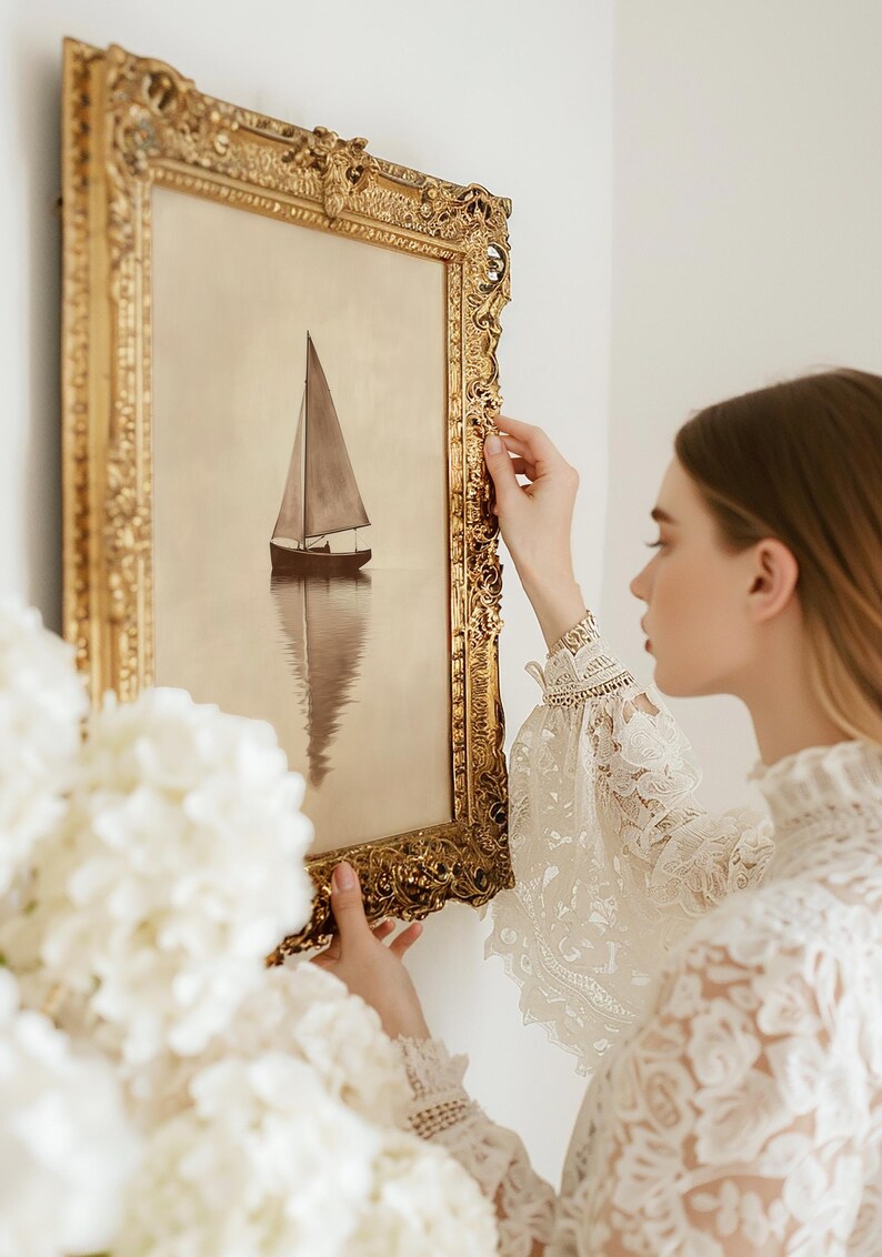 May include: A framed sepia-toned painting of a sailboat on calm water. The artwork is in an ornate, gold-colored frame. The image is being held up against a white wall.