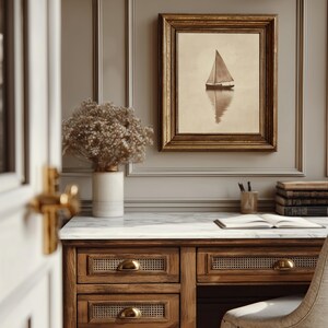 May include: A framed sepia-toned print of a sailboat on calm water hangs above a wooden desk. The desk has drawers with brass handles and a marble top. A vase of dried flowers sits on the desk.