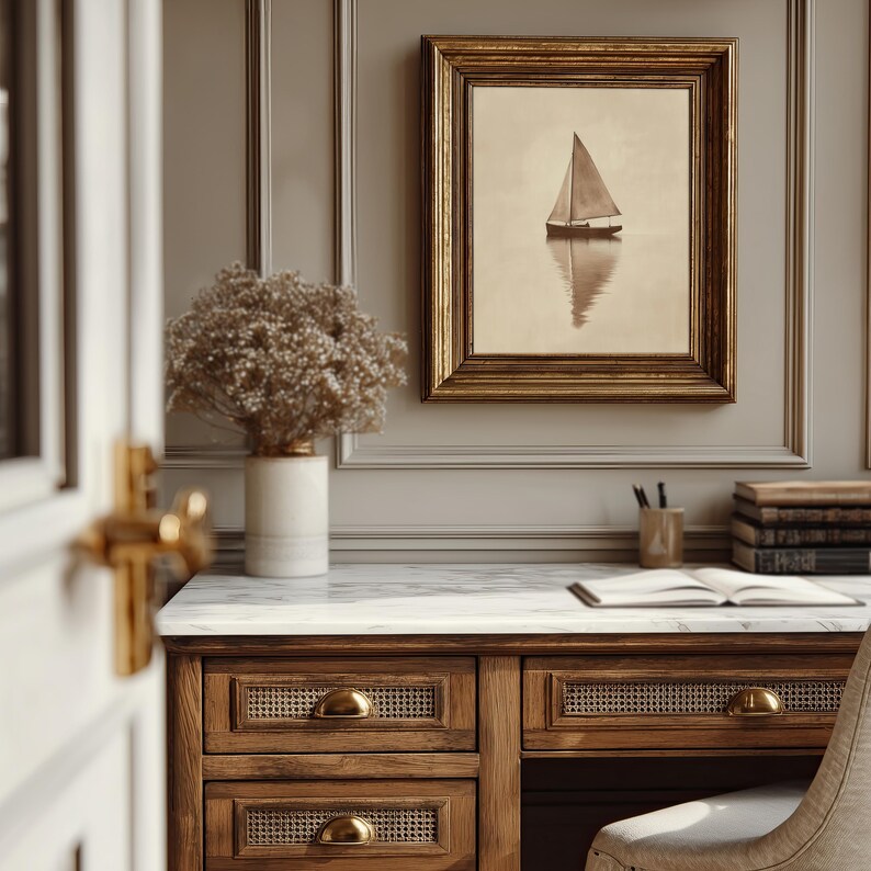 May include: A framed sepia-toned print of a sailboat on calm water hangs above a wooden desk. The desk has drawers with brass handles and a marble top. A vase of dried flowers sits on the desk.