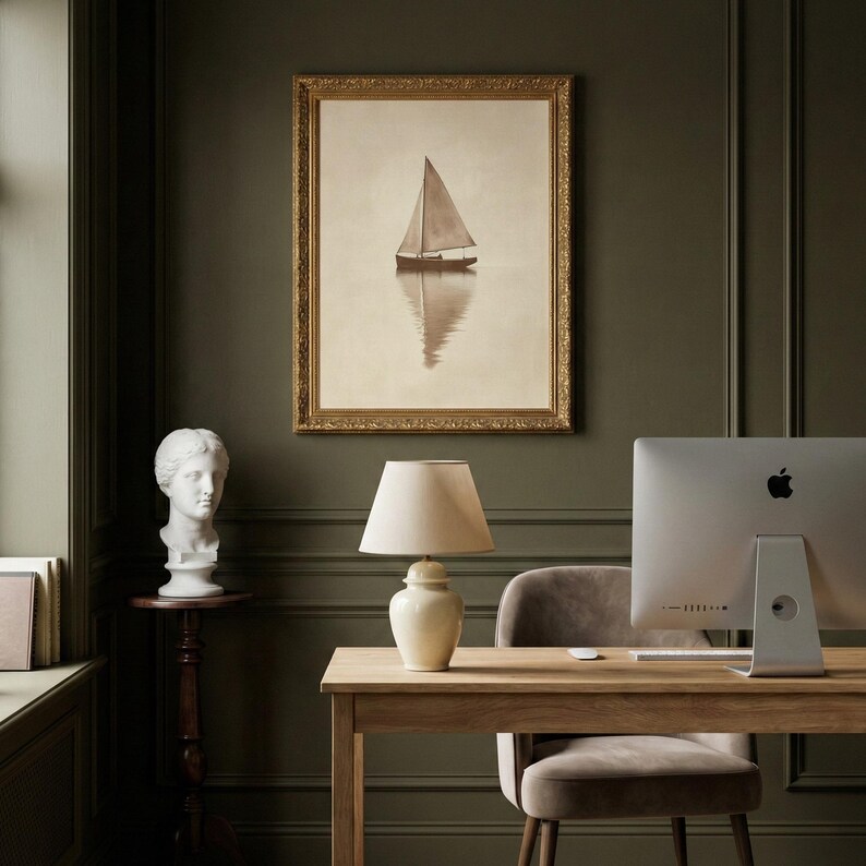 May include: A sepia-toned framed print of a sailboat on calm water hangs above a wooden desk. A white lamp with a beige shade sits on the desk, next to a computer. A white bust and a wooden side table are also in the room.