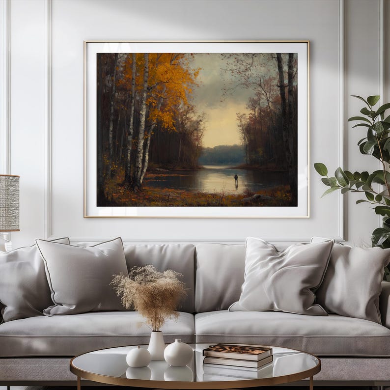 May include: A framed landscape painting depicting a calm lake surrounded by a dense forest with autumn foliage in shades of yellow and orange. A small, solitary figure stands near the water's edge under a soft, overcast sky with muted light.