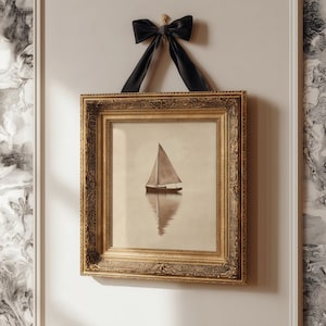 May include: A framed print of a sailboat on calm water, displayed with a gold ornate frame and a black velvet bow. The print has a sepia tone, and the frame is rectangular.