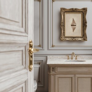 May include: A bathroom scene featuring a framed sailboat painting, a light wood vanity with a marble countertop, and gold fixtures. The walls are gray with decorative molding. A partially open white door with gold hardware is in the foreground.