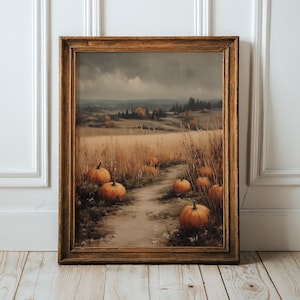 May include: A framed landscape painting depicting a dirt path winding through a field of tall, dry grass and orange pumpkins under a cloudy, overcast sky. The artwork is encased in a dark brown wooden frame with a textured, classic profile.