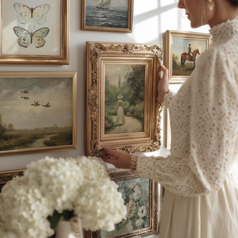 May include: A gallery wall featuring multiple framed artworks, including a central painting of a figure in a garden within an ornate gold frame, a butterfly print, a landscape with ducks, a seascape, and a horse rider, all arranged on a white wall.