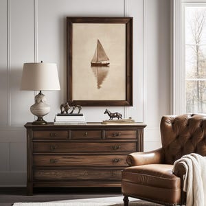 May include: A wooden dresser with multiple drawers and a framed sailboat art piece. A lamp with a beige shade sits on top of the dresser, along with decorative sculptures. A leather armchair and a window are in the background.