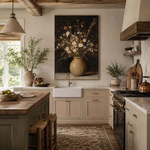 May include: A kitchen interior featuring a large framed painting of a floral bouquet in a tan vase above a white farmhouse sink. The space includes a wooden island, beige cabinetry, a black range, a copper kettle, and a patterned area rug.