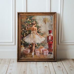 May include: A framed oil painting depicting a ballerina in a white tutu standing before a decorated Christmas tree with gold ornaments and a star. A red nutcracker stands to the right, and wrapped gift boxes are placed on the floor below.
