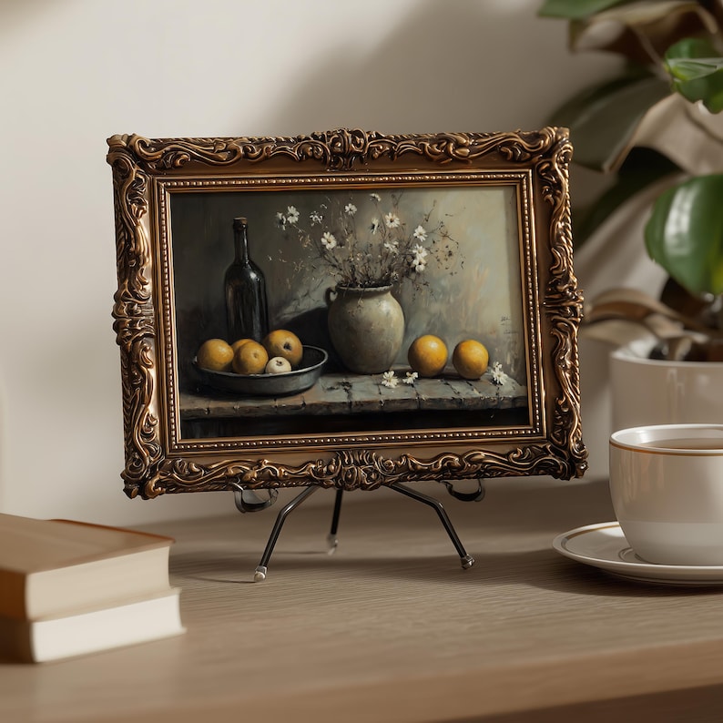 May include: A rectangular painting in an ornate, dark gold-toned frame resting on a metal easel. The artwork depicts a still life scene featuring a dark bottle, a ceramic vase with white flowers, and several yellow fruits on a wooden surface.