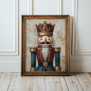 May include: A framed oil painting of a nutcracker figure wearing a gold crown with a red jewel, a red jacket with gold trim, and a white beard. The nutcracker has a black mustache, blue eyes, and a textured, neutral-toned background.