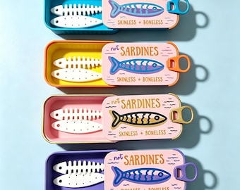 May include: Four rectangular metal tins with sliding lids, each labeled "not SARDINES SKINLESS + BONELESS" with a fish illustration. Inside each tin are two white, flat, fish-shaped objects, one a skeleton and one a solid piece with dots.