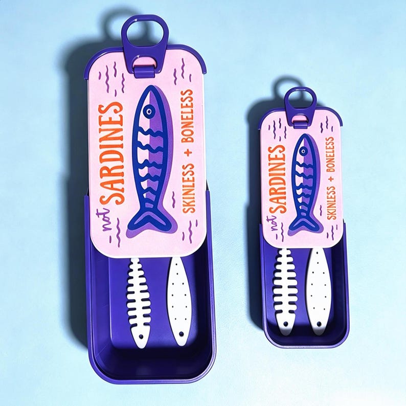 Puede incluir: Dos recipientes rectangulares de color morado con tapas deslizantes que presentan un panel superior rosa claro. Las tapas muestran un gr&aacute;fico de pez azul oscuro, el texto "not SARDINES" y "SKINLESS + BONELESS" y una leng&uuml;eta de apertura.