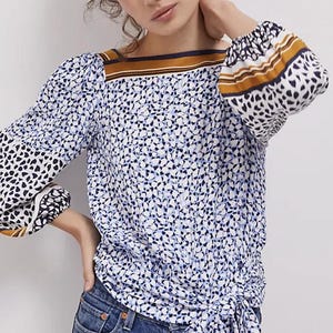 Puede incluir: Una blusa de manga larga con un estampado floral azul y blanco. La blusa presenta un escote cuadrado con una raya marr&oacute;n y azul marino, y las mangas tienen un estampado de coraz&oacute;n en blanco y negro. La blusa est&aacute; atada a la cintura.