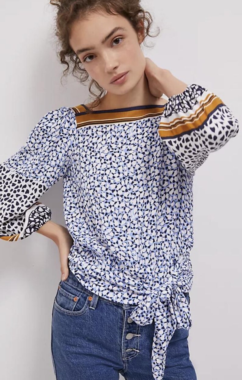 Puede incluir: Una blusa de manga larga con un estampado floral azul y blanco. La blusa presenta un escote cuadrado con una raya marr&oacute;n y azul marino, y las mangas tienen un estampado de coraz&oacute;n en blanco y negro. La blusa est&aacute; atada a la cintura.
