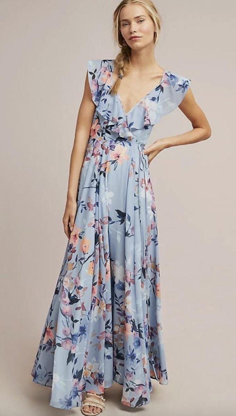 May include: A light blue floral print maxi dress with a V-neckline and ruffled trim. The dress features a flowing skirt and a delicate floral pattern in shades of pink, purple, and blue. The dress is floor-length.