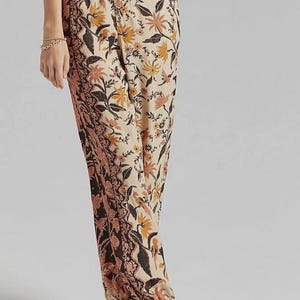 Puede incluir: Pantalones con estampado floral en beige, marr&oacute;n y naranja. Los pantalones presentan un patr&oacute;n floral detallado con un dise&ntilde;o de borde contrastante. Se combinan con sandalias negras. El estilo es bohemio y casual.