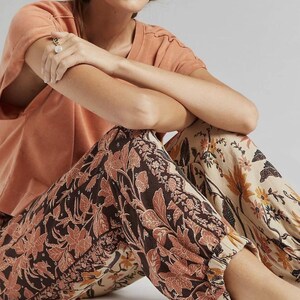 Puede incluir: Una persona con una camiseta color melocot&oacute;n y pantalones con estampado floral. Los pantalones presentan un estampado floral marr&oacute;n oscuro y melocot&oacute;n sobre un fondo crema. Los pantalones tienen pu&ntilde;os el&aacute;sticos en los tobillos.