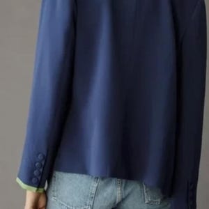 May include: A navy blue blazer with a white and green trim on the collar and cuffs. The blazer has three buttons on each cuff. The model is wearing denim shorts.