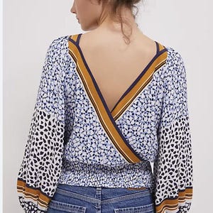Puede incluir: Una blusa estampada con dise&ntilde;o de cuello en V. La parte superior presenta un estampado floral azul y blanco en el cuerpo y manchas negras y blancas en las mangas. Las mangas son largas y terminan con una raya marr&oacute;n y blanca. La blusa se combina con vaqueros azules.