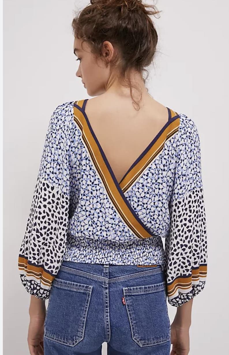 Puede incluir: Una blusa estampada con dise&ntilde;o de cuello en V. La parte superior presenta un estampado floral azul y blanco en el cuerpo y manchas negras y blancas en las mangas. Las mangas son largas y terminan con una raya marr&oacute;n y blanca. La blusa se combina con vaqueros azules.