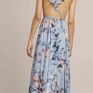 May include: A light blue floral print maxi dress with a low back and ruffled cap sleeves. The dress features a flowing skirt and a delicate floral pattern in shades of pink, purple, and blue.