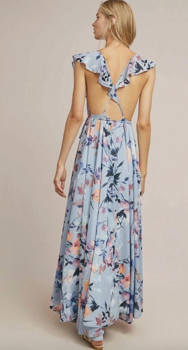 May include: A light blue floral print maxi dress with a low back and ruffled cap sleeves. The dress features a flowing skirt and a delicate floral pattern in shades of pink, purple, and blue.