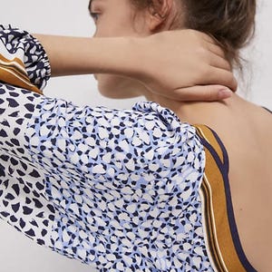 Puede incluir: Top estampado con mangas largas. La tela presenta un dise&ntilde;o de formas blancas, azul marino y celeste. El escote y los pu&ntilde;os de las mangas tienen un detalle de rayas marrones y azul marino. La espalda del top est&aacute; abierta.